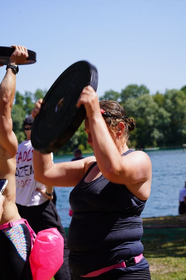 A Deadly Swim racer pressing a weight plate overhead by the lake